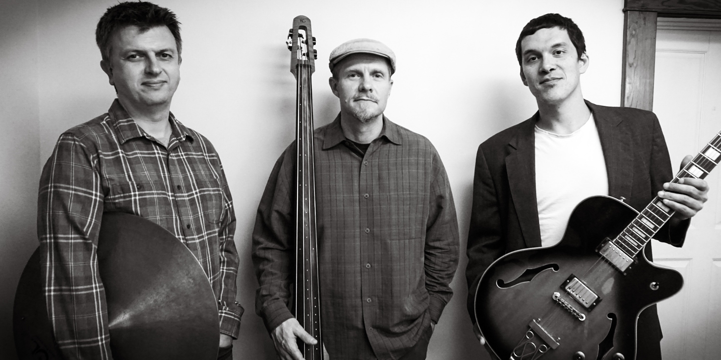Black and white photograph of the house trio: Three men standing. One in the middle holds an upright bass. One on the right holds a guitar.