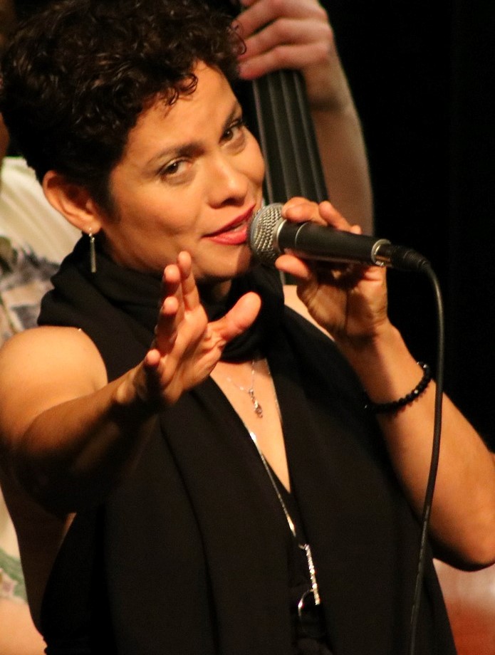 Maria Rodriquez singing into a microphone and holding out her right hand