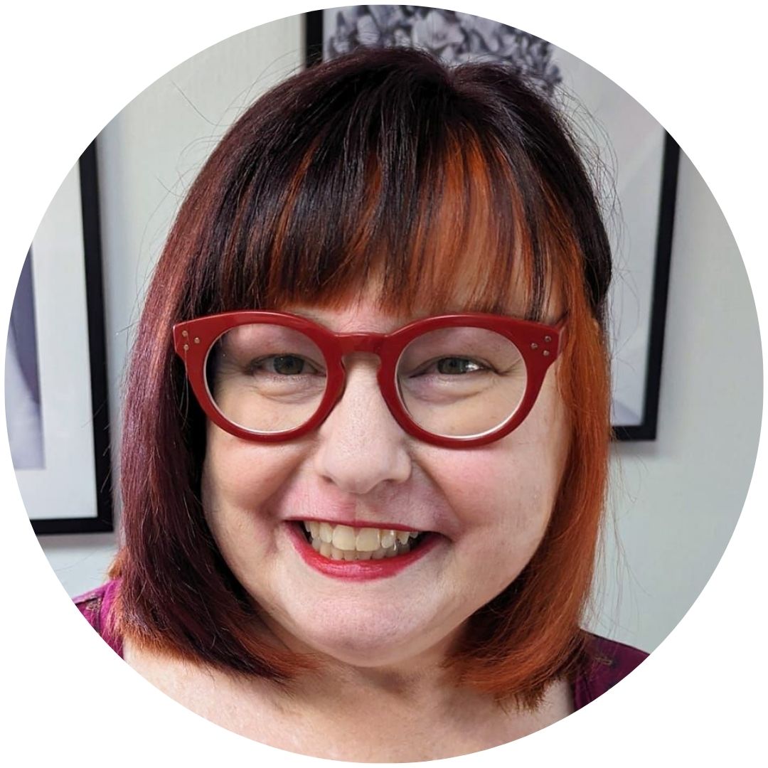 A color headshot of a woman with red hair and red glasses smiling into the camera.