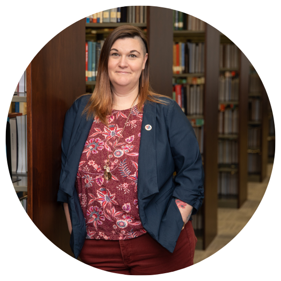 woman leaning against a bookshelf in a library with more bookshelves behind her