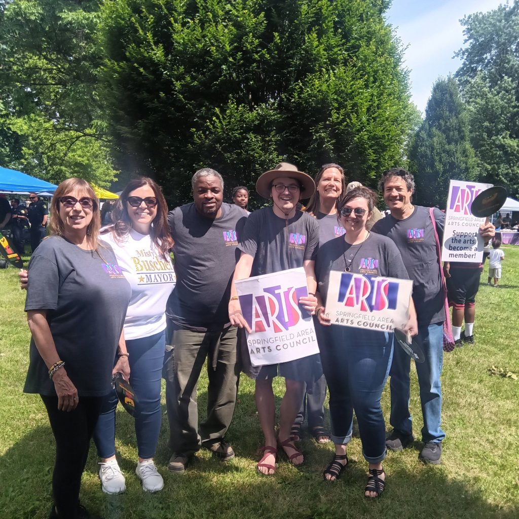 group of seven people posing in a park with trees holding signs