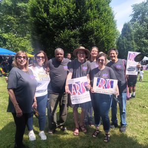 group of seven people posing in a park with trees holding signs