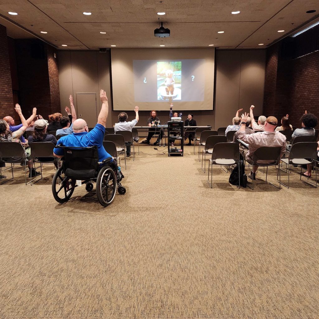 group of people sitting in meeting room with a projector raising their hands.