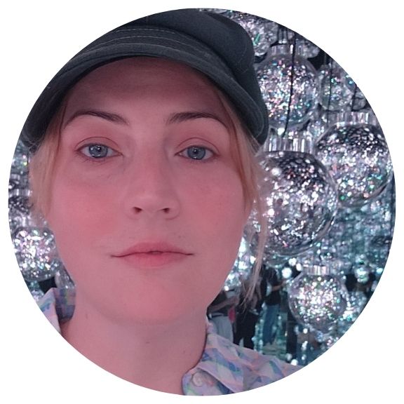 selfie of a woman with short blond hair wearing a cap in front of a silvery background