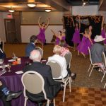 Group of dancers performing in front of a crowd of people seated at round tables