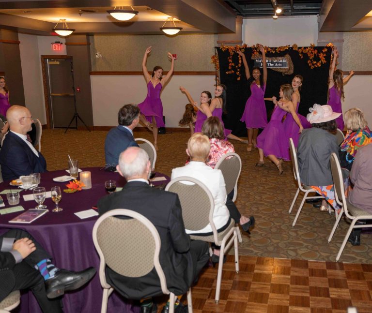 Group of dancers performing in front of a crowd of people seated at round tables