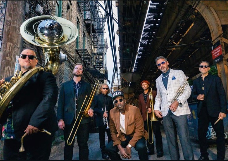 band of 7 musicians standing in an ally with instruments