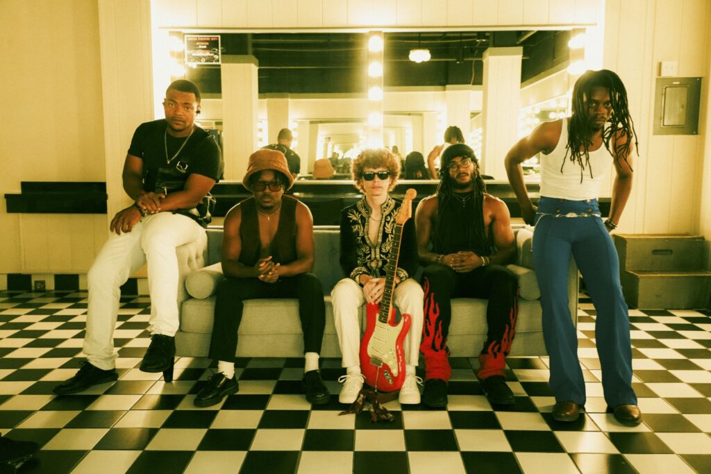 band of musicians posed in a greenroom with a guitar